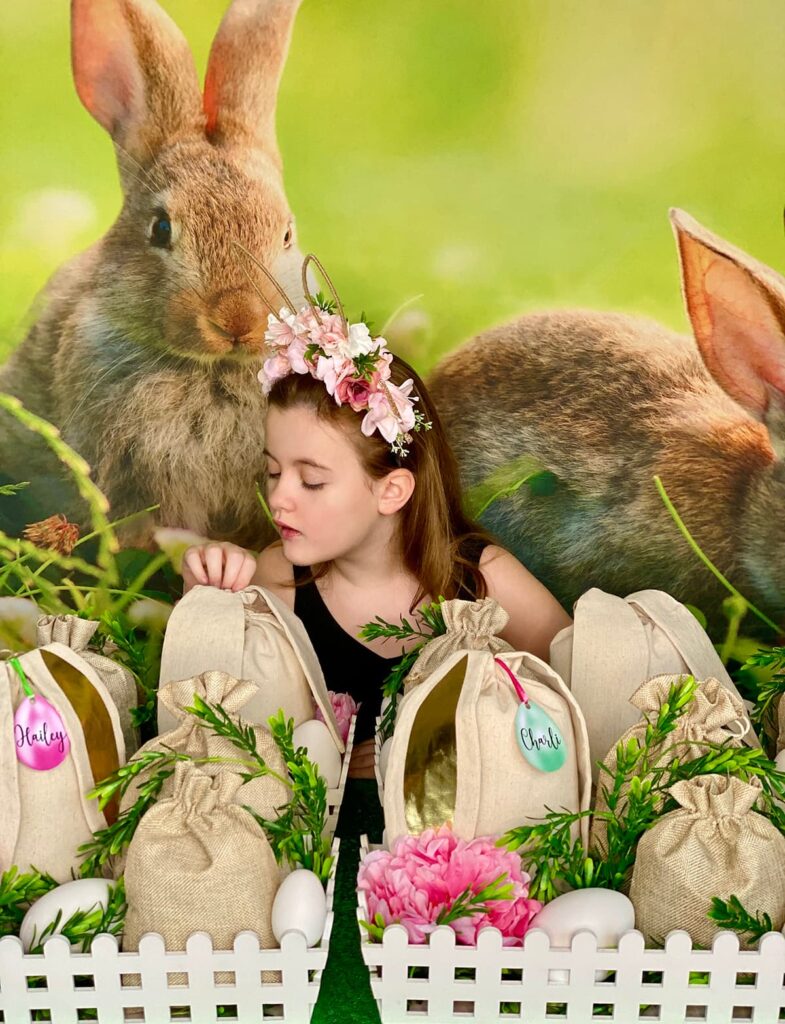 Child sitting at Easter fairy garden party table, touching a hessian bunny ear bag and looking at it with anticipation.