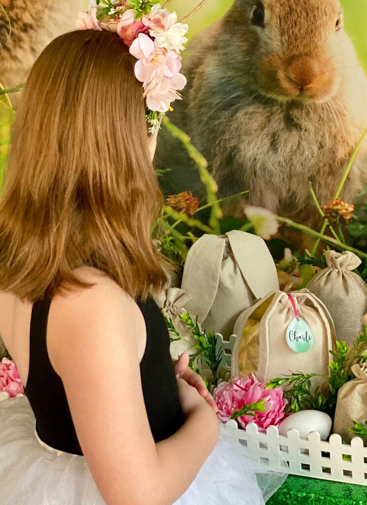 Girl at Easter fairy garden party table with craft supplies, hessian bags, greenery, and bunny backdrop.
