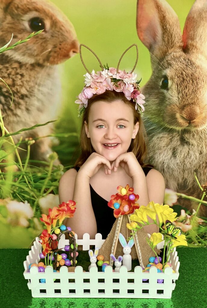 Child smiling and almost laughing happily while showing the camera her completed Easter fairy garden crate.