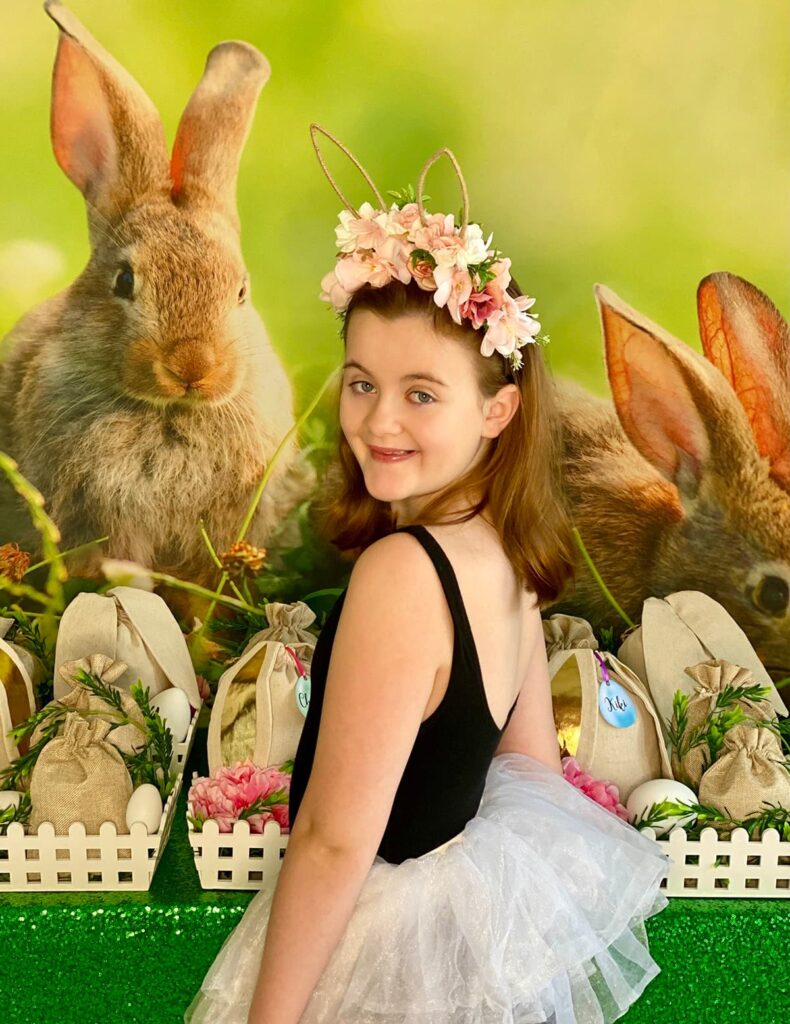 Young girl smiling over her shoulder at the camera at an Easter fairy garden party with spring decorations in the background.