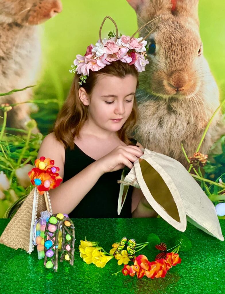 Child unpacking craft supplies from a hessian bunny ear bag at an Easter fairy garden party table, with items spread out on the table.