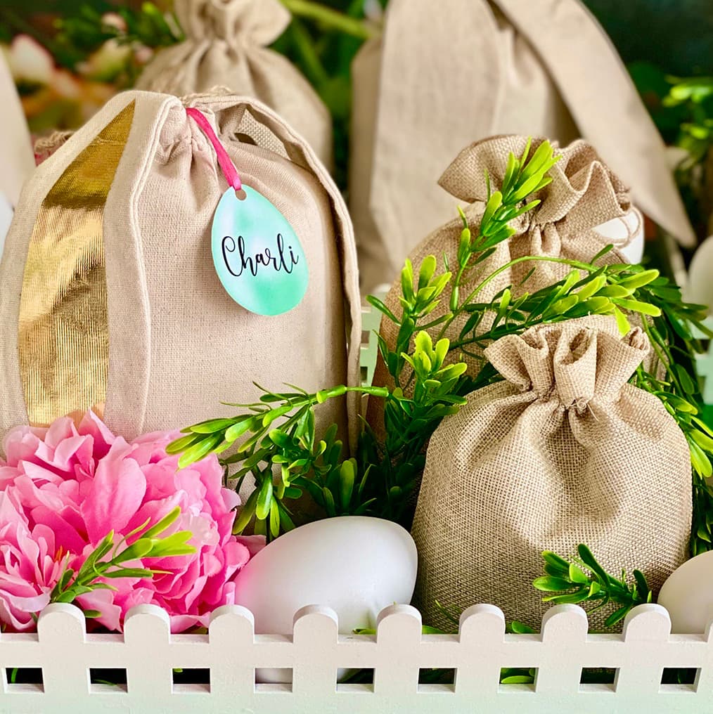Close-up of an Easter Fairy Garden activity crate featuring a hessian supply bag, faux greenery, pink flower, plastic egg, and a visible egg-shaped name tag.