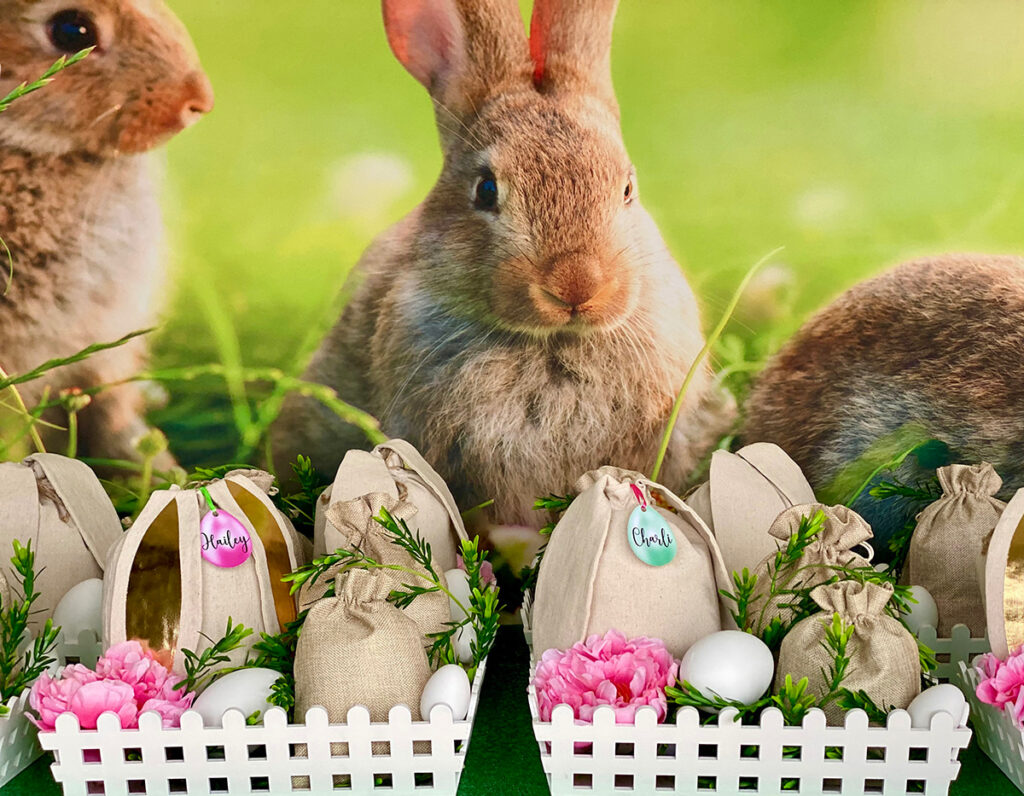 Multiple white Easter fairy garden crates with hessian bags, faux greenery, plastic white eggs, and floral accents in front of a bunny-themed backdrop.