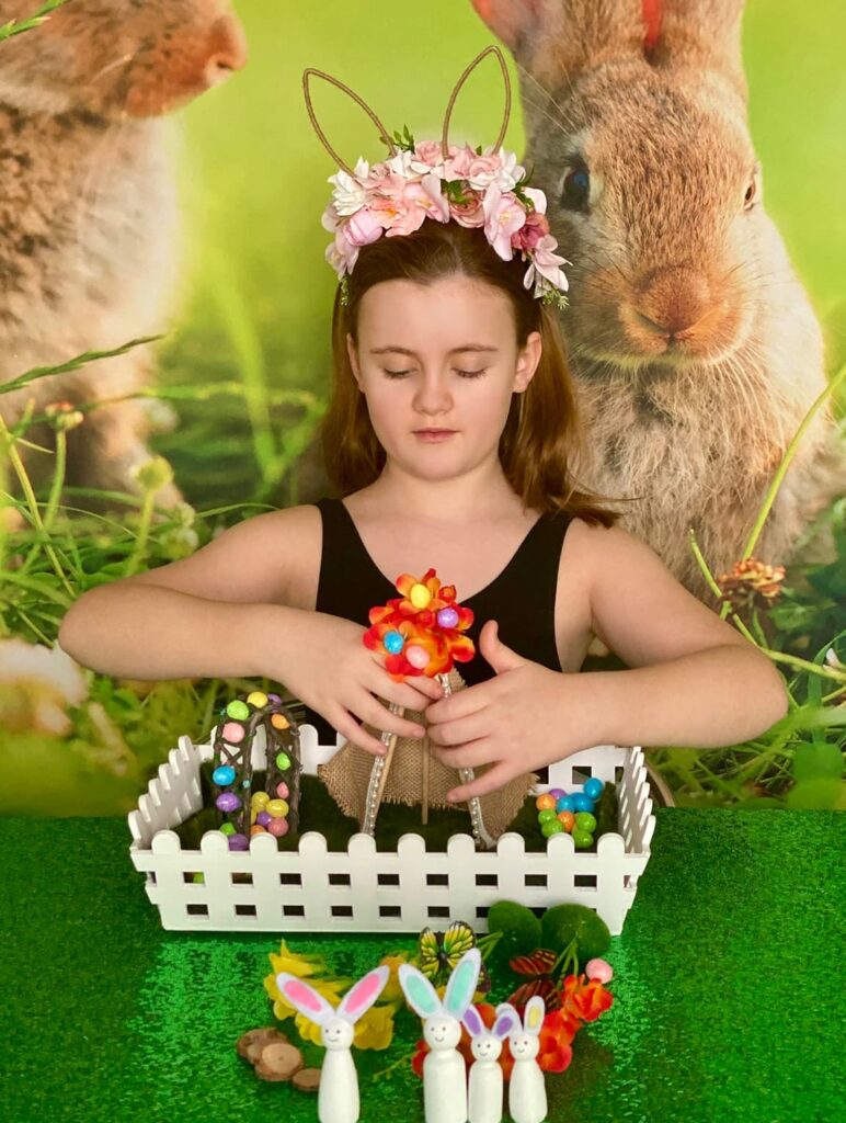 Child carefully separating the legs of a miniature fairy teepee to secure it to the base of the Easter fairy garden crate.