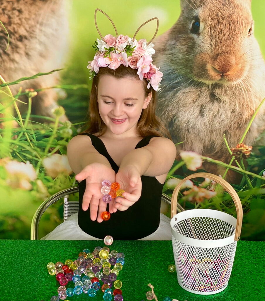 Smiling girl pouring bright, colorful acrylic beads from her hands onto the table for an Easter basket decorating activity.
