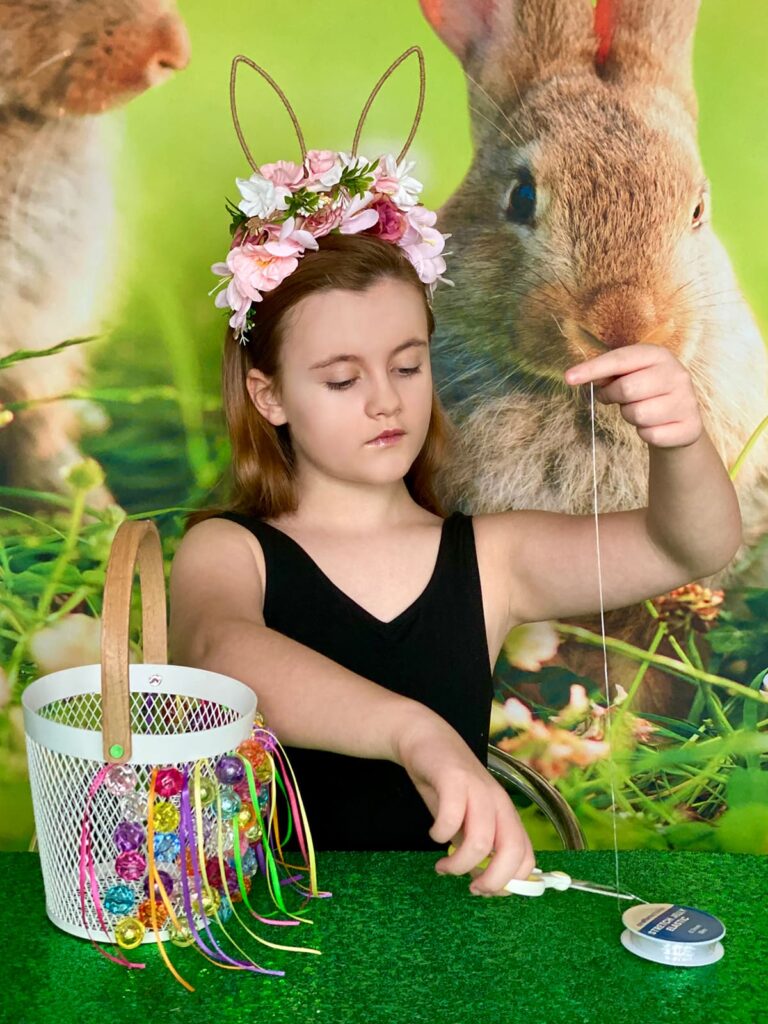 Girl cutting a piece of elastic to use for threading beads and attaching them to her Easter basket during the decorating activity.