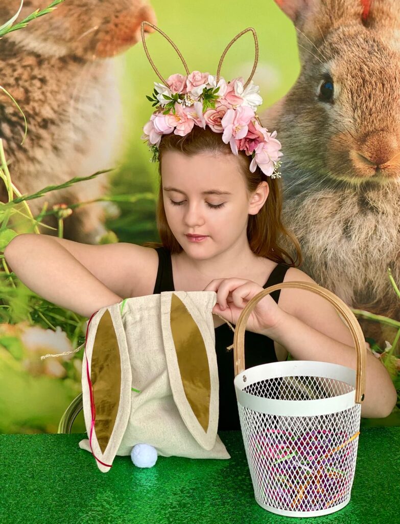 Young girl reaching into a bunny ear bag, ready to pull out Easter basket decorating supplies.