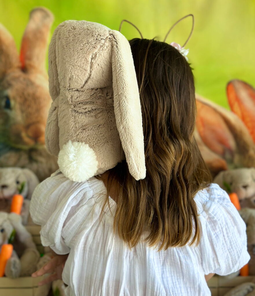 Close-up of a girl with her back to the camera, holding an Easter Bunny plush on her shoulder in front of an Easter Bunny Adoption table.