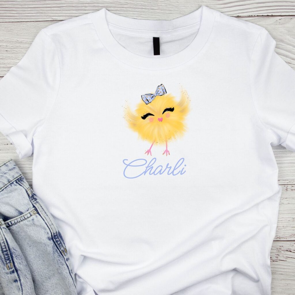 Personalized white t-shirt featuring a cute yellow chick and the name "Charli," designed as a matching party outfit for an Easter chick-themed celebration from Inspired Party Merch.