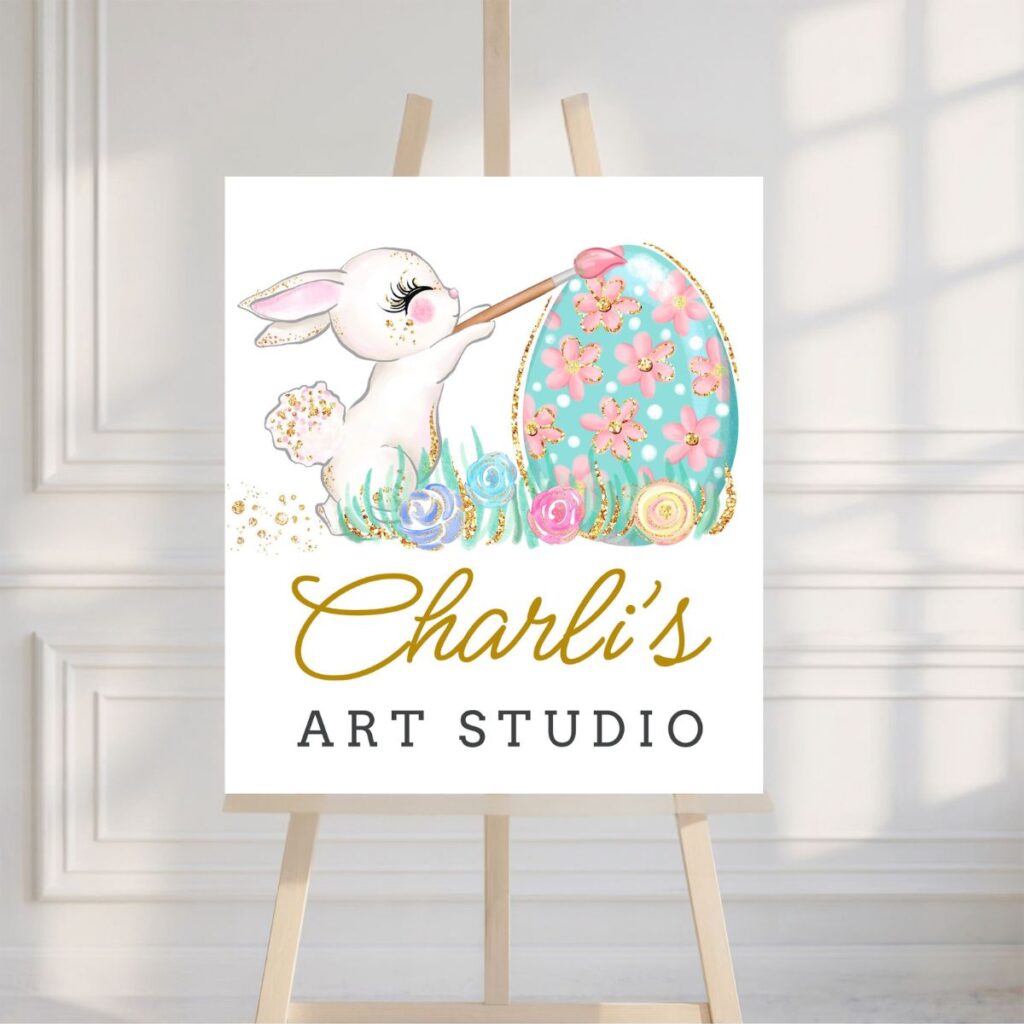 Printable Easter Art Studio sign displayed on a wooden easel in front of a white wall, from Inspired Party Design.