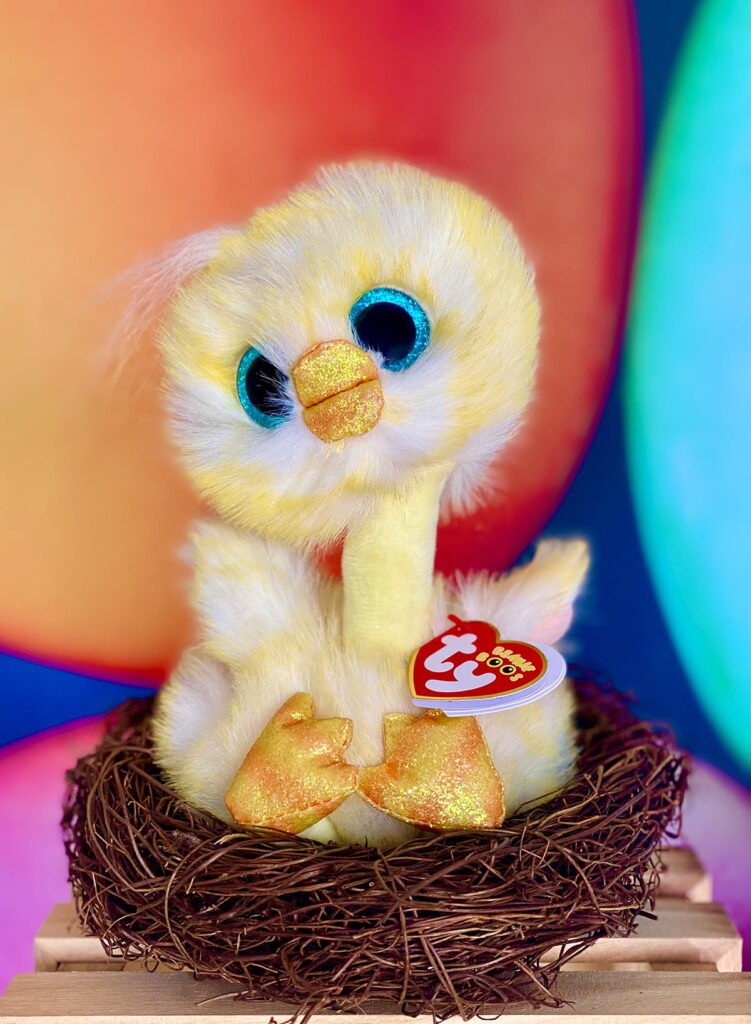 Adorable plush Easter chick nestled in a faux nest with a different angle of the vibrant Easter egg-themed background, creating a cheerful springtime vibe.