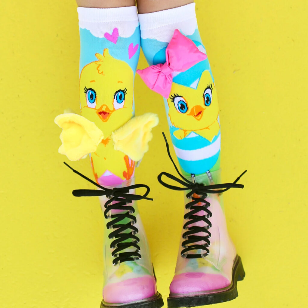 Child’s legs from knee down wearing colorful Mad Mia chick socks and bright boots against a yellow background.