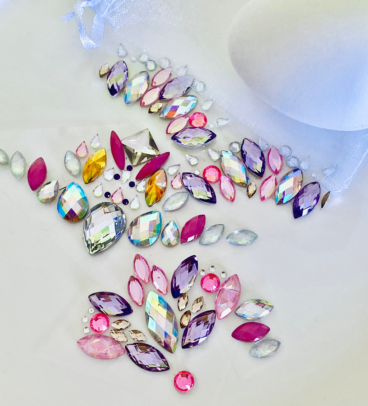 Beautiful face gem stickers laid out on a table, with a white plastic Easter egg and a glimpse of a white organza bag, showcasing the supplies for the craft.