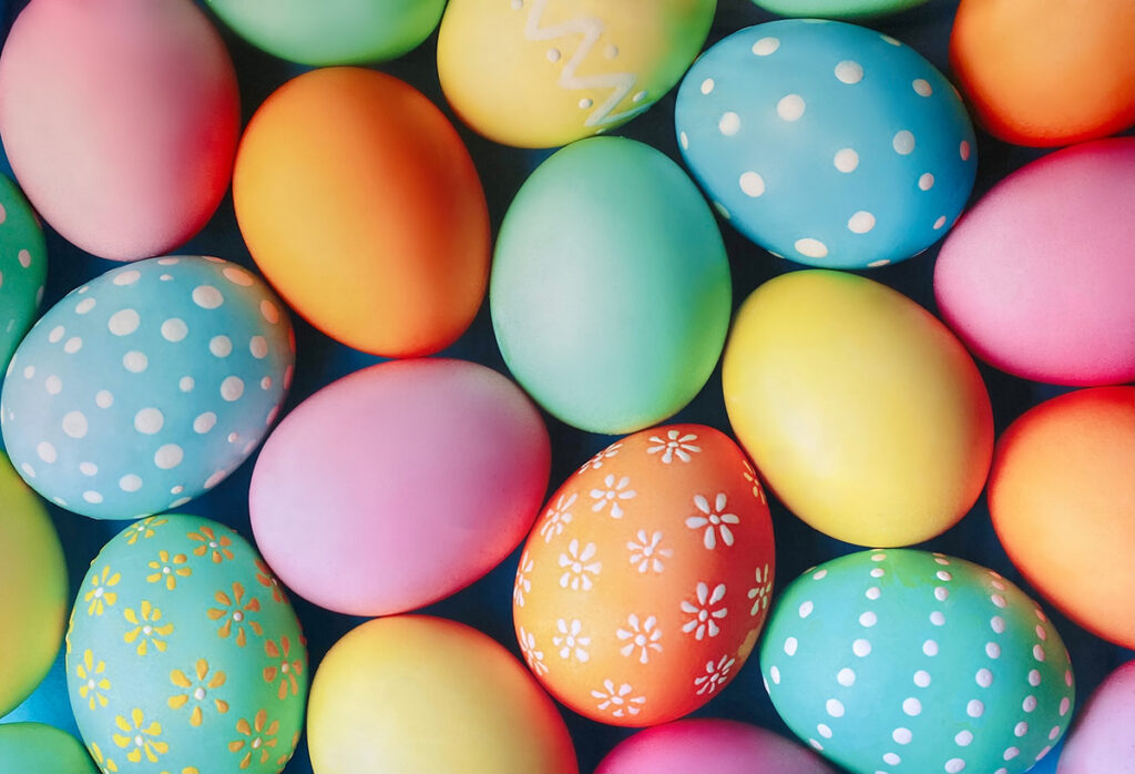 Close-up of a vibrant Easter egg backdrop showing a colorful pattern of decorated eggs in pastel and bright hues.