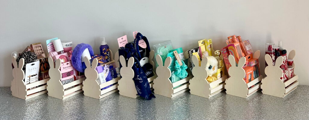 Angled view of eight colorful bunny-shaped wooden crates showcasing their wooden ends and themed kids’ beauty party favours, arranged on a silver sequin tablecloth.