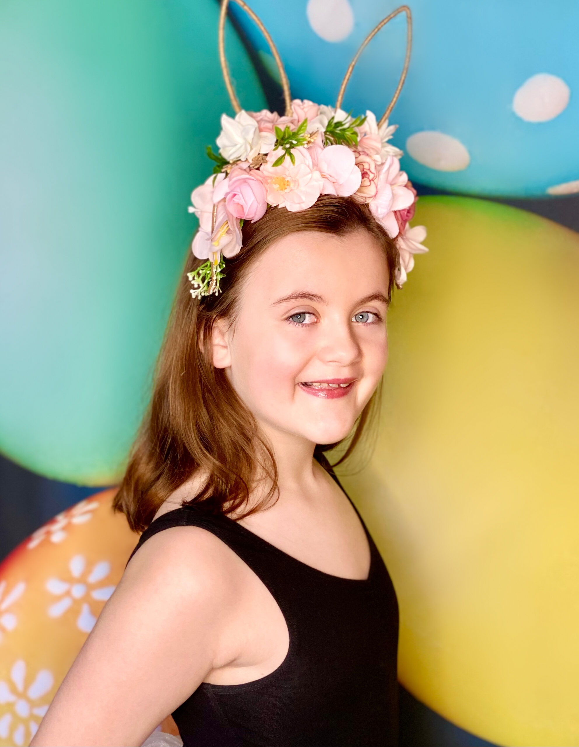 Beautiful young girl enjoying an Easter party with a vibrant, colorful Easter egg backdrop behind her.