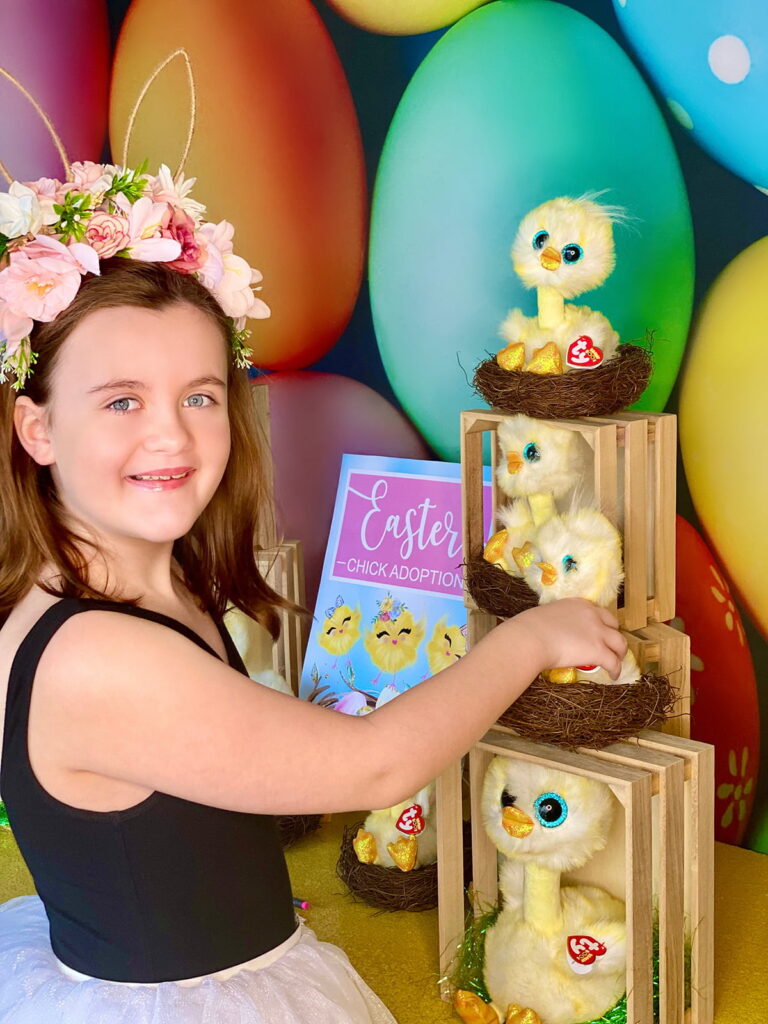 Young girl smiling at the camera with her hand on her chosen plush chick at the chick adoption party table.