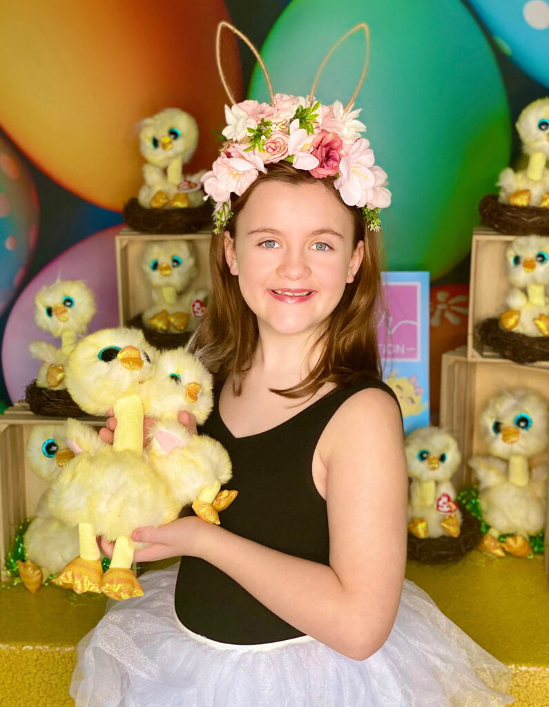 Happy young girl standing in front of the Easter Chick Adoption party table, smiling brightly while holding two plush Easter chicks in her hands.