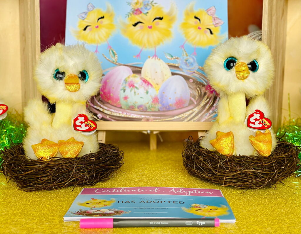 Two plush Easter chicks nestled in faux nests, displayed in front of an “Easter Chick Adoption” sign with printed adoption certificates placed behind them, creating an adorable and official setup for the party activity.