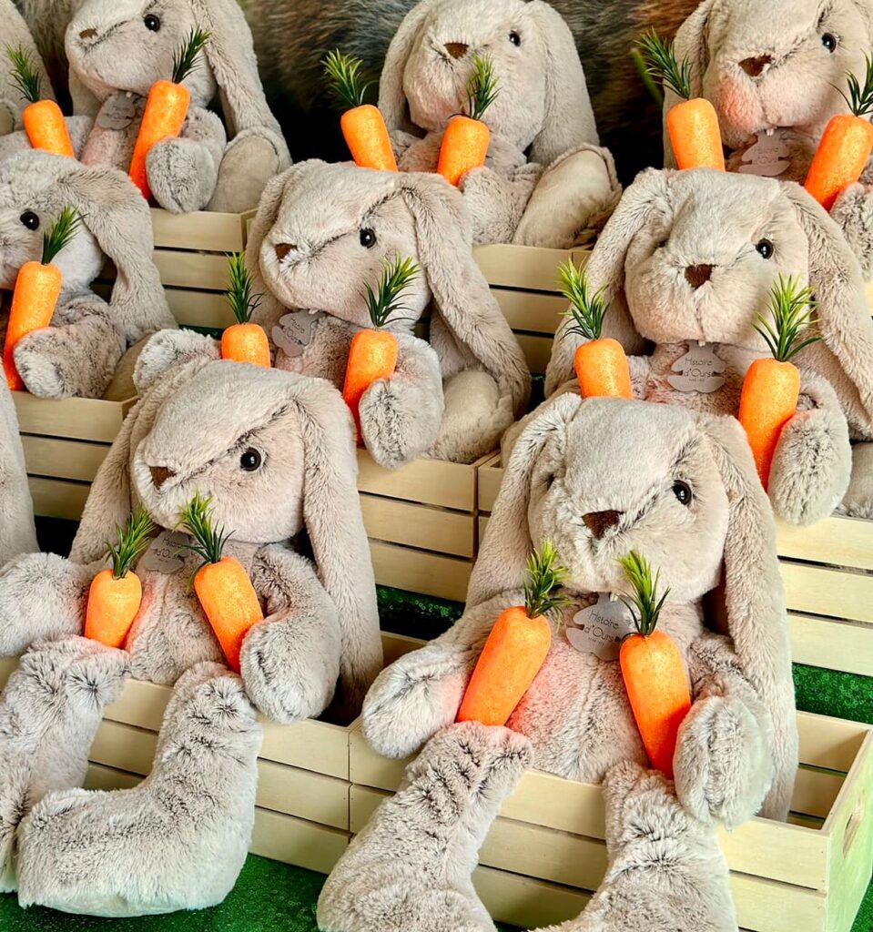 Side angle view of plush bunnies arranged in three staggered rows, each nestled in small wooden crates with colourful foam carrots, creating a charming Easter display.