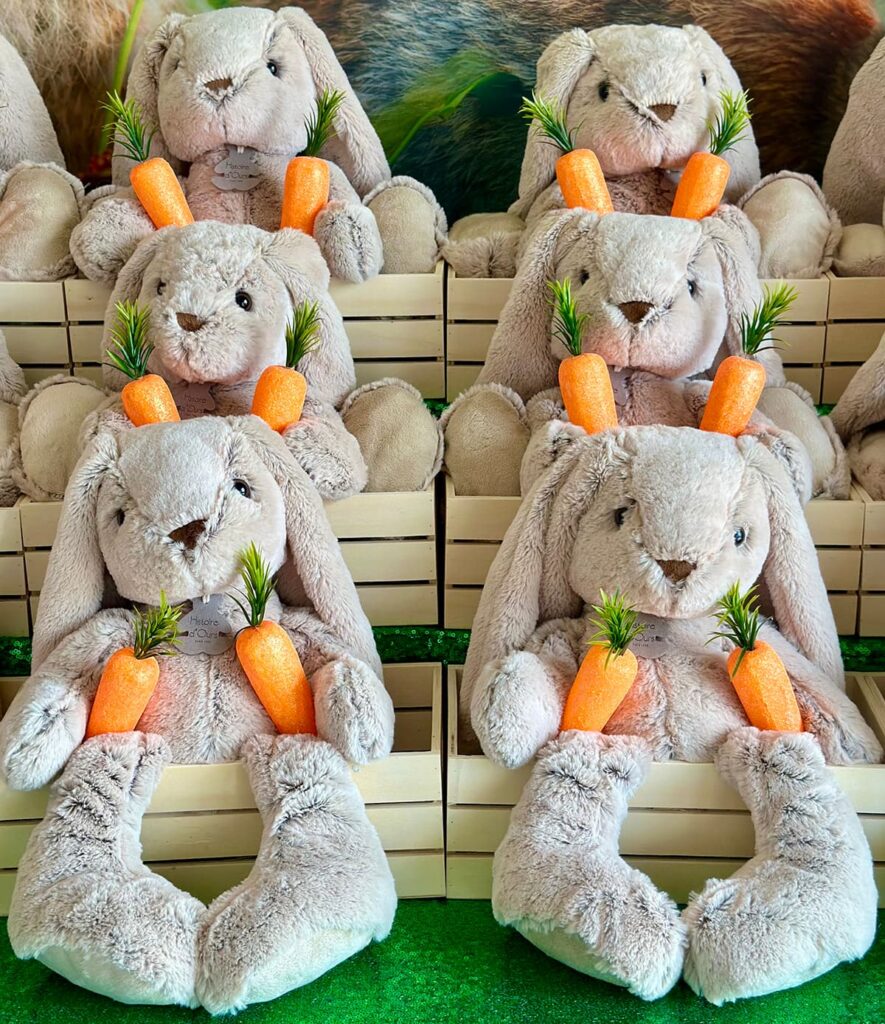 Six plush bunnies sitting in wooden crates arranged at staggered heights like stairs, each crate filled with faux carrots.