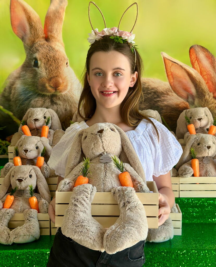 Smiling girl standing in front of the Bunny Adoption table, holding a crate with a plush bunny and faux carrots.
