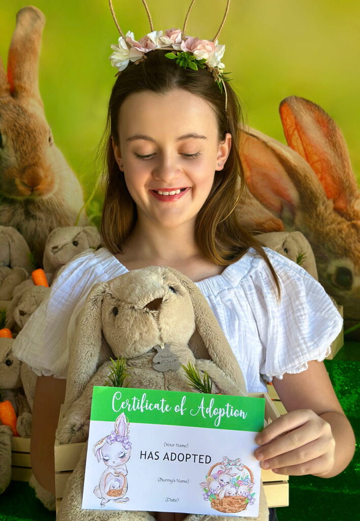 Smiling girl holding an Easter Bunny Adoption crate filled with a plush bunny, while holding the adoption certificate in front.