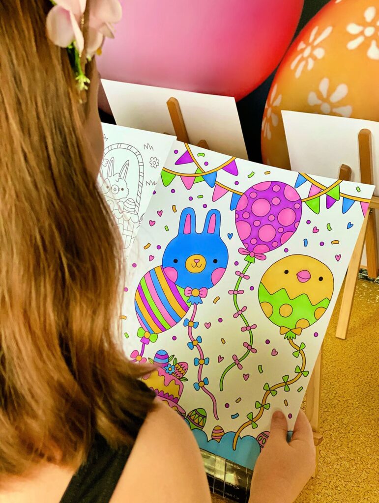 Overhead view of young girl holding a completed Easter colouring poster at the Easter party activity table.