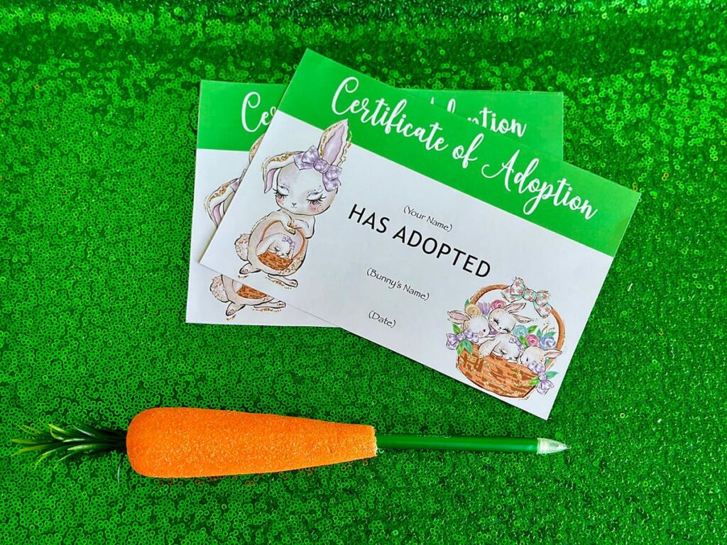 Two Easter Bunny Adoption certificates displayed on a green sequin tablecloth with a carrot-shaped pen beside them.