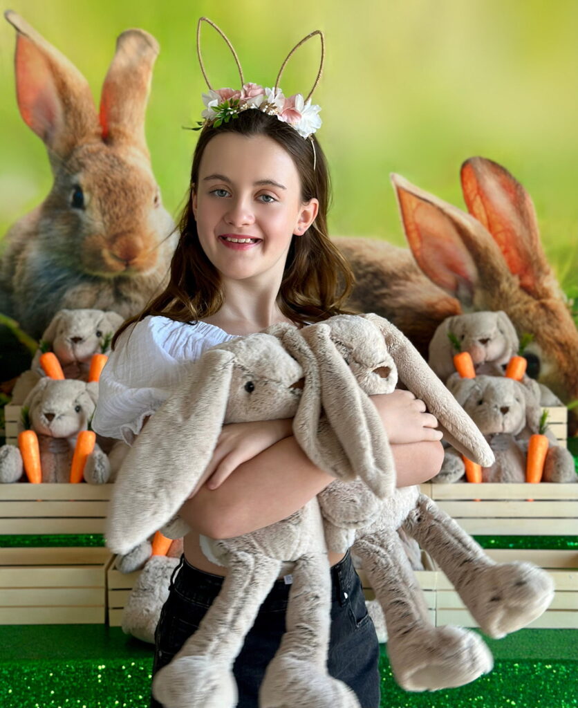 Young girl smiling and holding two plush bunnies to her chest while standing in front of an Easter Bunny Adoption table.