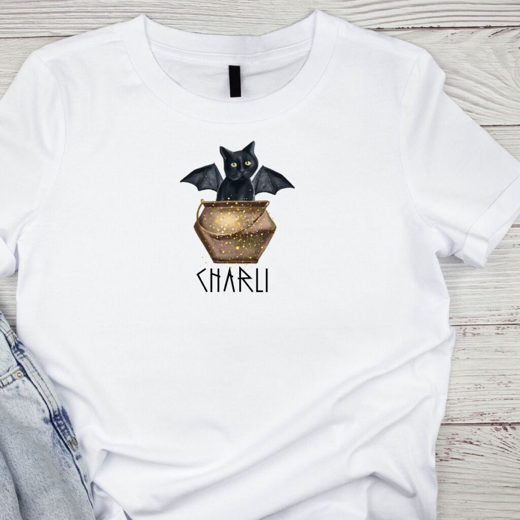 White t-shirt from Inspired Party Merch featuring a gold cauldron with black cat peeking out and personalised name, perfect for DIY cauldron party.