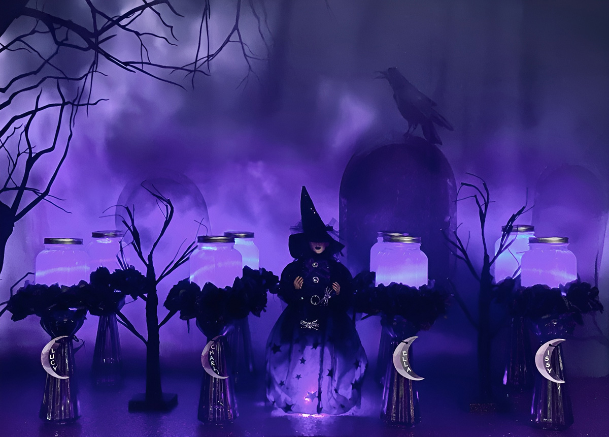 DIY witch lantern party table with glowing purple mason jars, witch centerpiece, black LED trees and moon name tags.