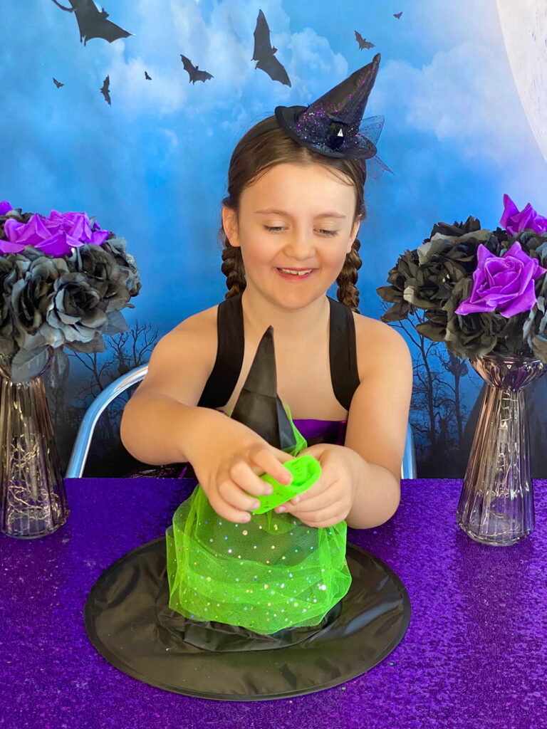 Young girl smiling as she wraps green tulle around her black DIY witch hat during a party craft activity.