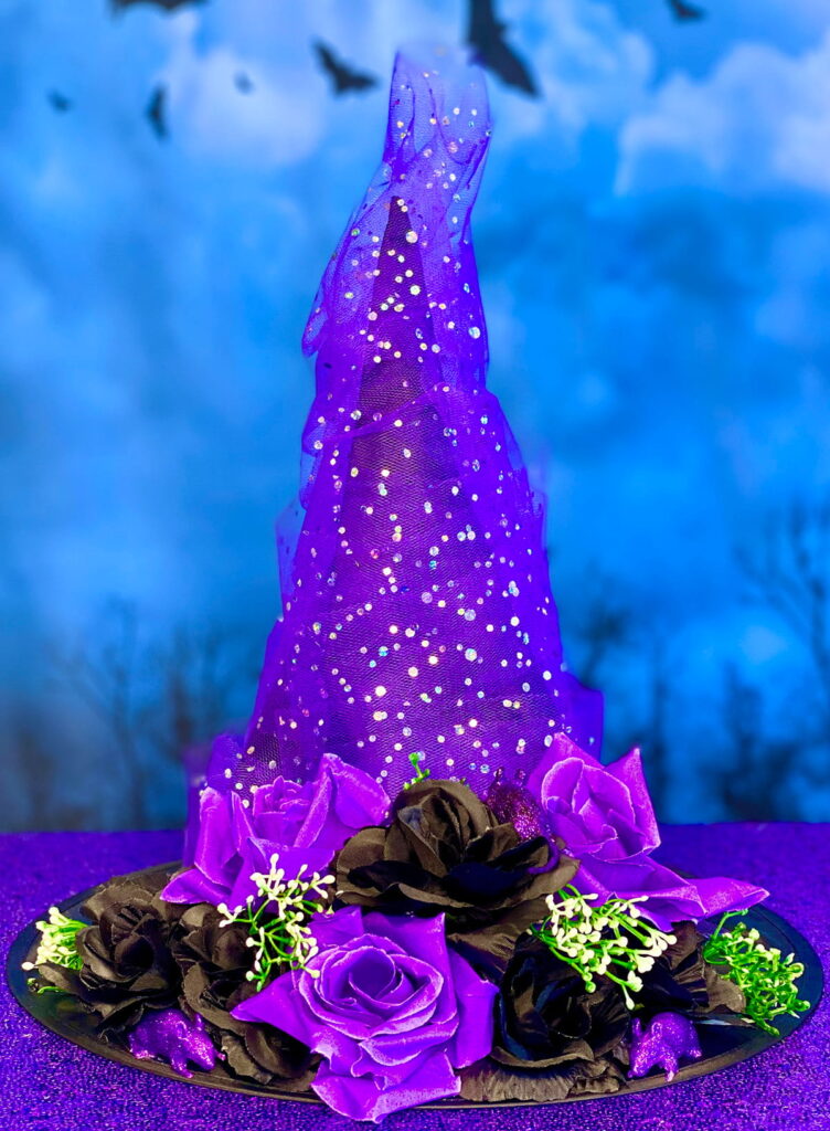 Purple floral DIY witch hat displayed on a table, decorated with glittery purple tulle and black and purple roses on the brim.
