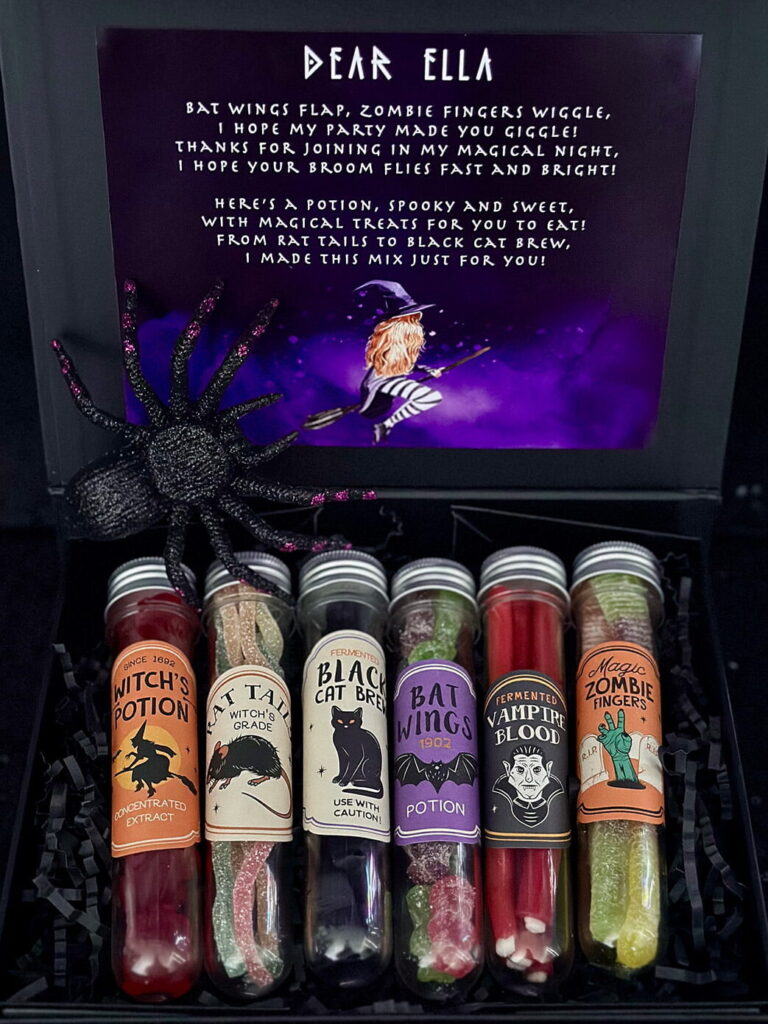 Sweet Spells witch party favours with plastic potion vials filled with candy, including sour spaghetti rat tails and red gummy frogs, displayed in a black box with a glitter spider decoration.
