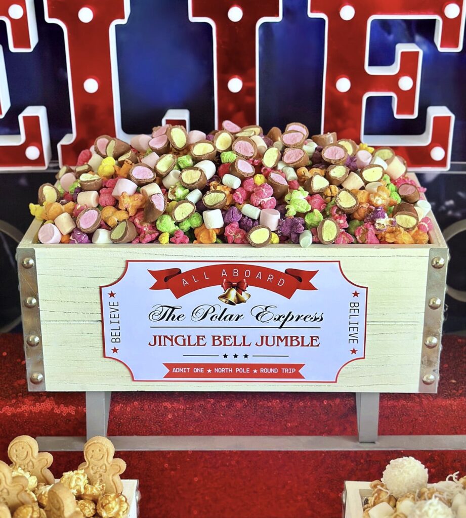 Close-up of Christmas Jingle Bell Jumble popcorn in a Santa sleigh crate with a train ticket-style label for a kids’ Polar Express popcorn bar.
