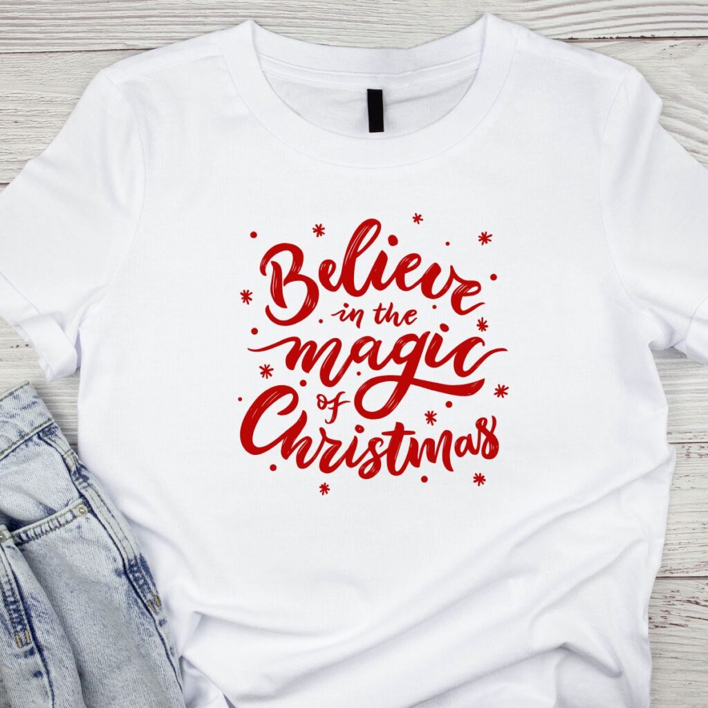 White t-shirt reading “Believe in the magic of Christmas” in red letters, promoting Inspired Party Merch shop.