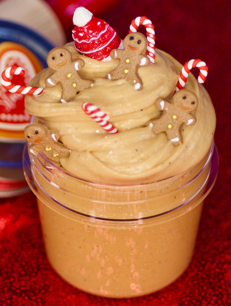 Close-up of gingerbread-coloured, scented slime in a clear jar with Christmas-themed resin charms for the kids’ Christmas slime party activity.