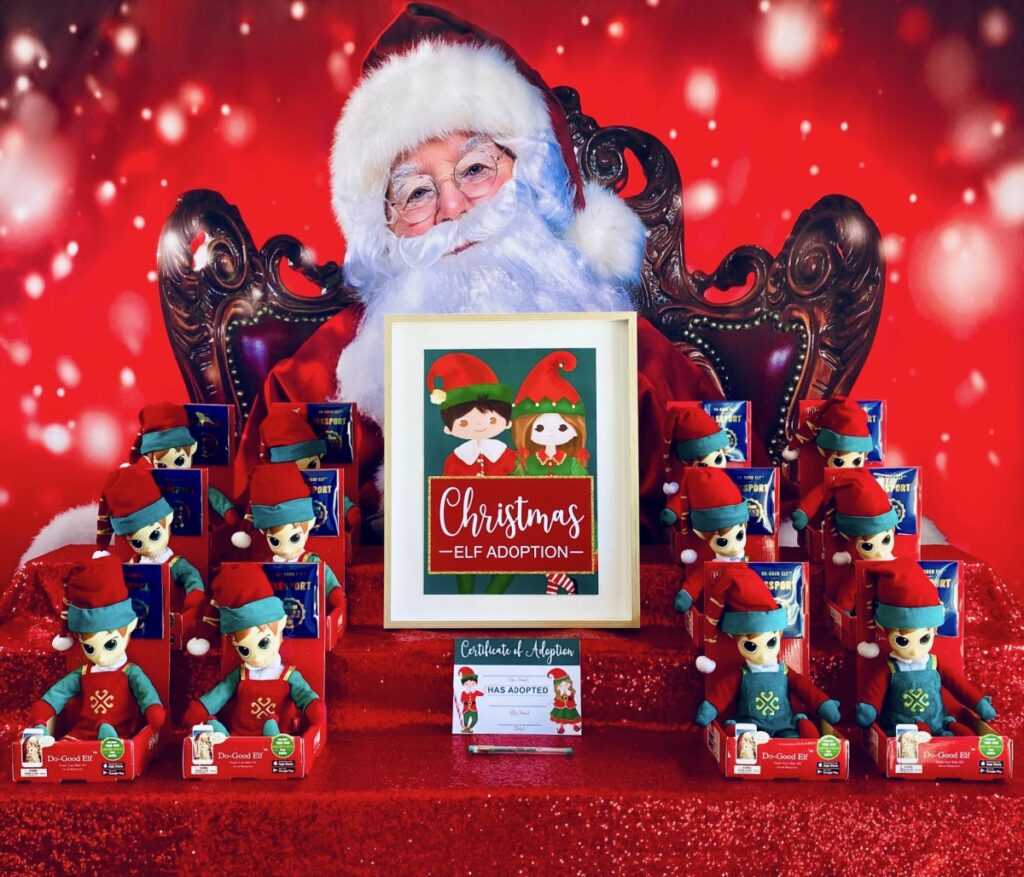 Elf adoption kids’ Christmas party activity table with Santa backdrop, red sequin tablecloth, and North Pole elves with adoption sign.