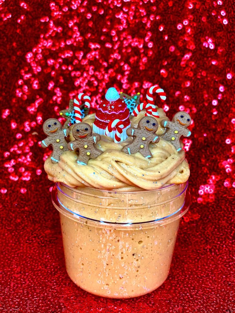 Completed Christmas slime in clear jar with gingerbread men and Christmas-themed resin charms, displayed on red sequin tablecloth.
