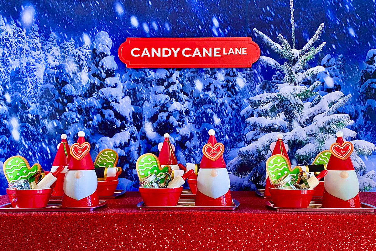 Kids’ Christmas slime party table setup with snowy winter backdrop, red sequin tablecloth, silver trays, Santa jars of slime supplies, and red bowls with cookie cutters and rolling pin for cookie slime activity.
