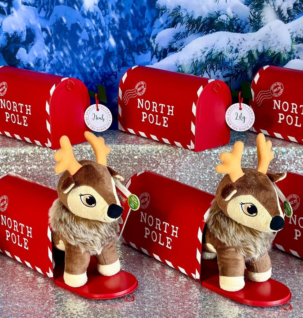 Red North Pole post box party favours with plush reindeer peeking out, displayed for a kids’ Christmas party.