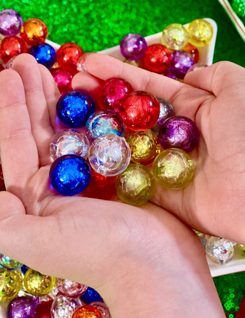 Colourful Christmas jewelry beads in the palms of hands, inspired by holiday baubles for a kids’ jewelry-making activity.