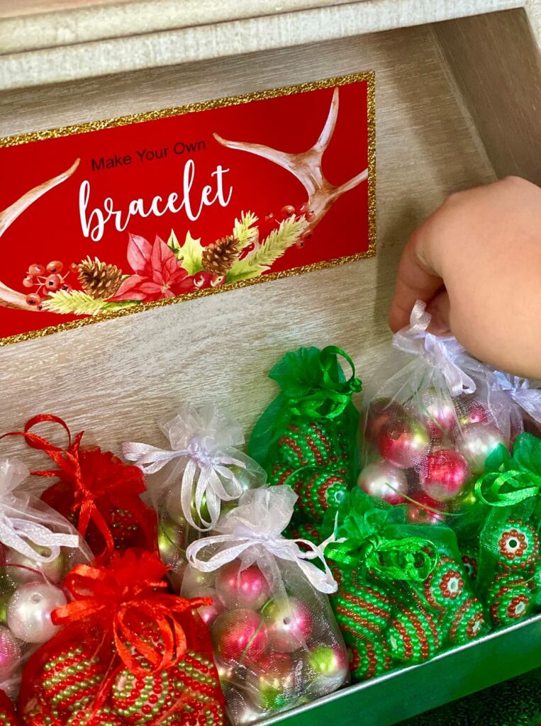 DIY Christmas floating locket kits on display with a sign, as a young girl’s hand reaches to pick one up.