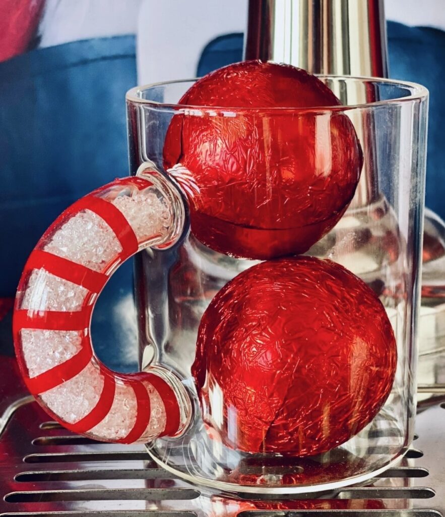 Christmas hot cocoa bombs wrapped in red foil in a clear mug with a candy cane-striped handle.