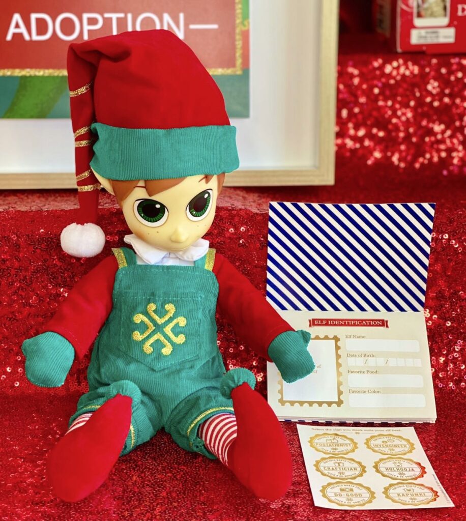 Portable North Pole plush elf on the party table with an elf passport and stickers for the kids’ adoption activity.