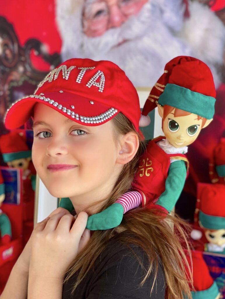 Plush elf perched on a child’s shoulders during an elf adoption party, showing the elf’s playful expression from behind the child.