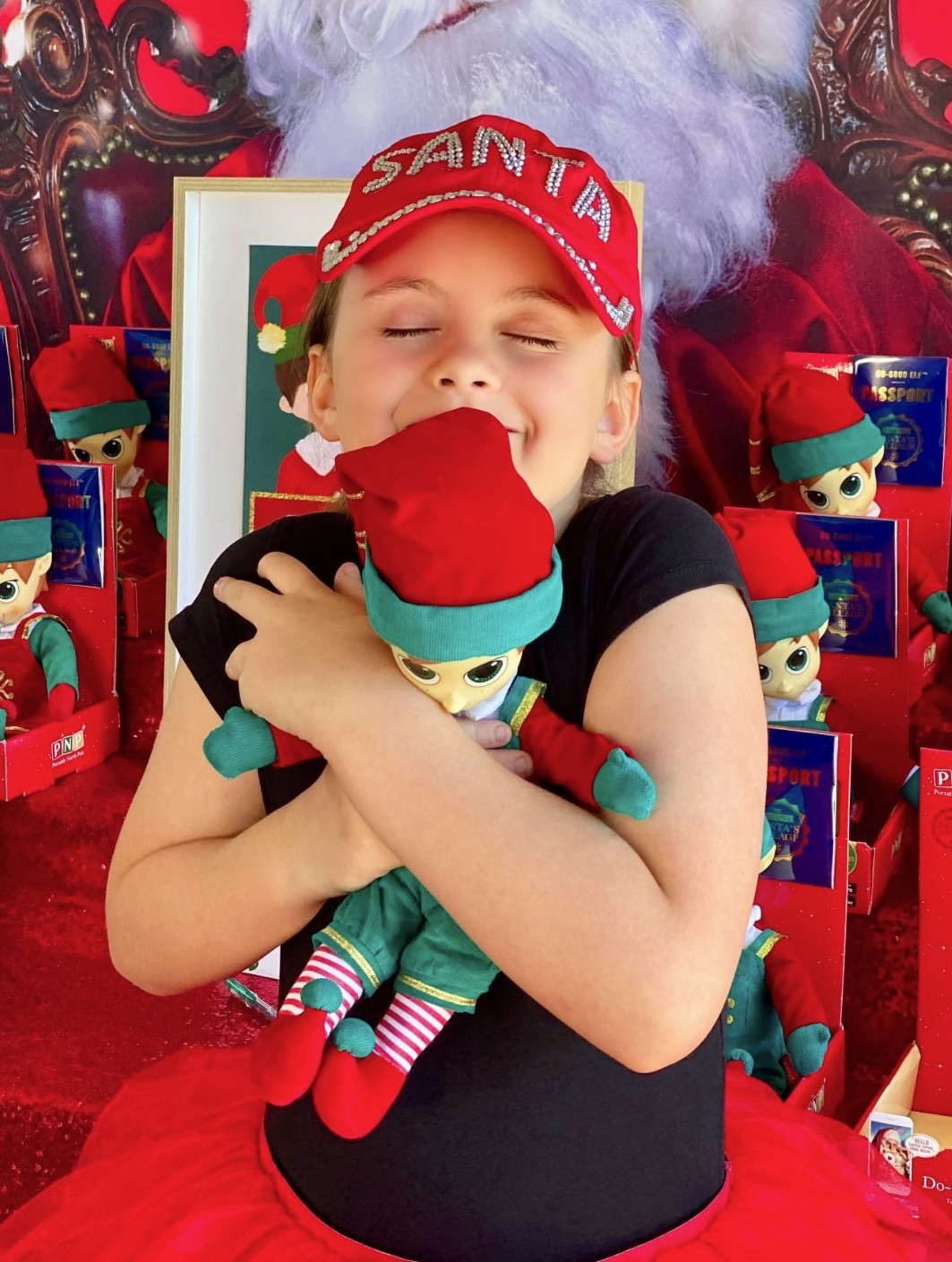 Young girl hugging her Christmas elf tightly to her chest and smiling in front of the elf adoption party table.