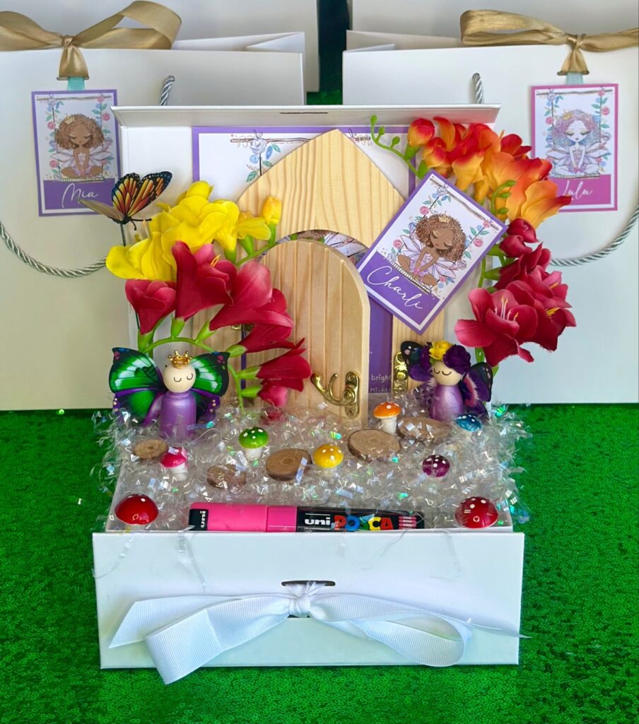 DIY fairy door kit party favour for kids with wooden door, Posca paint pens, faux flowers and wooden fairies in a white gift box on iridescent shred with thank you card and personalised name tag.