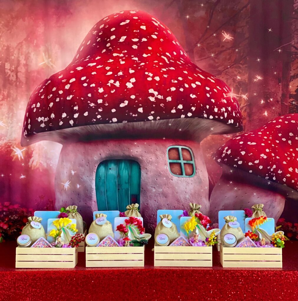 Fairy bread slime party table with red mushroom backdrop, red sequin tablecloth and wooden crates of slime supplies including mixing bowls and take-home jars.